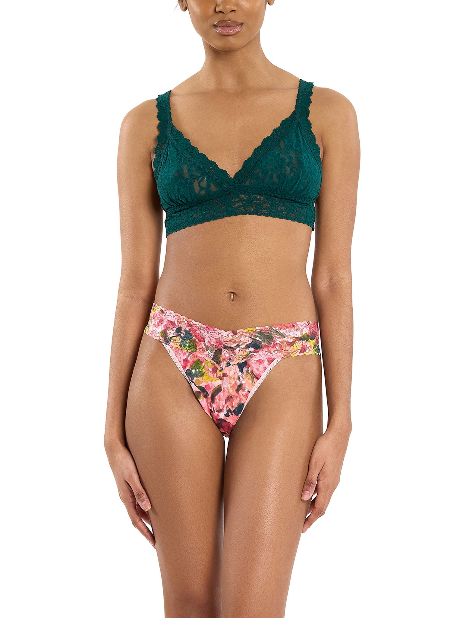 woman wearing floral pink lace thong with dark green bra standing in front of white background