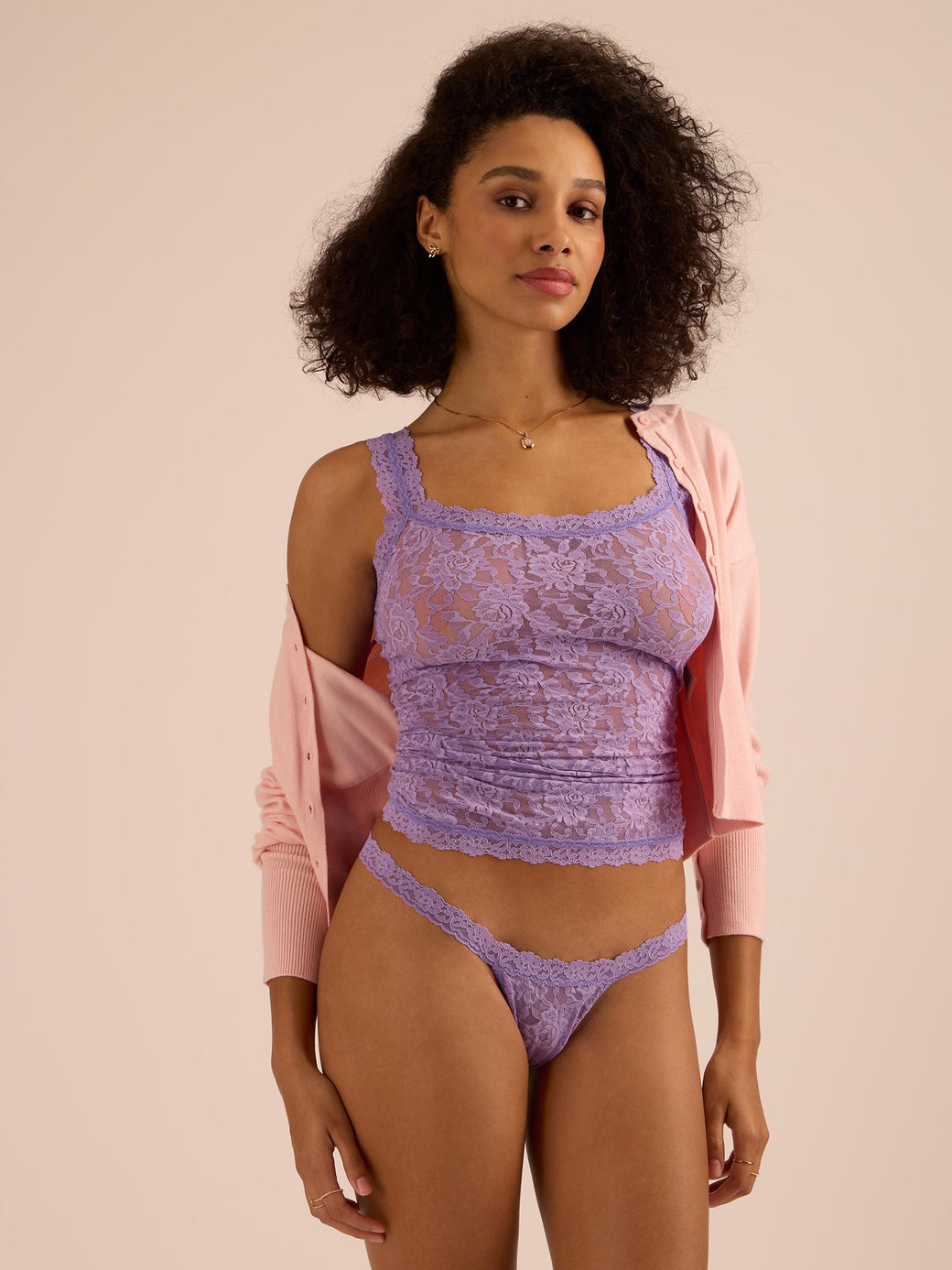 Woman wearing a purple lace top and underwear set with a pink cardigan on a beige background