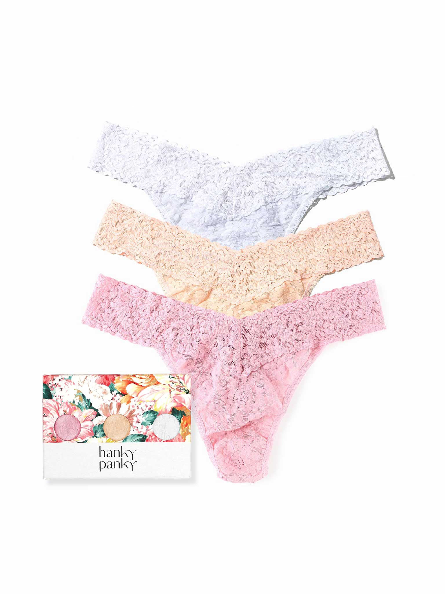Three pairs of lace panties in white, beige, and pink with a floral gift box on a white background.