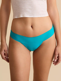 Person wearing turquoise bikini bottoms and a white top on a beige background