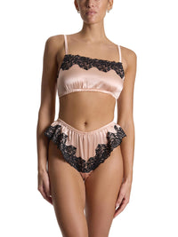 Woman wearing a blush pink and black lace lingerie set on a white background