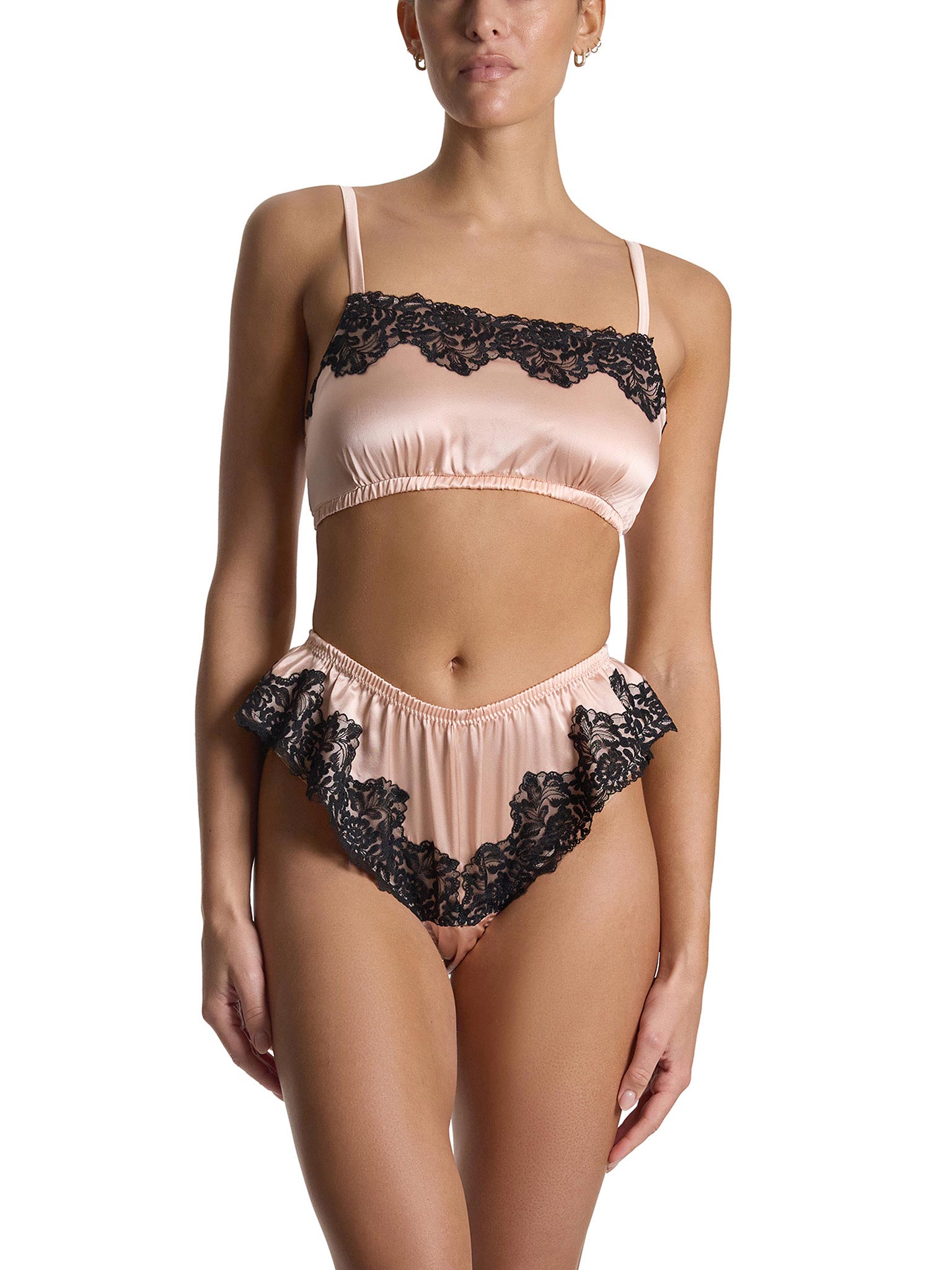 Woman wearing a blush pink and black lace lingerie set on a white background