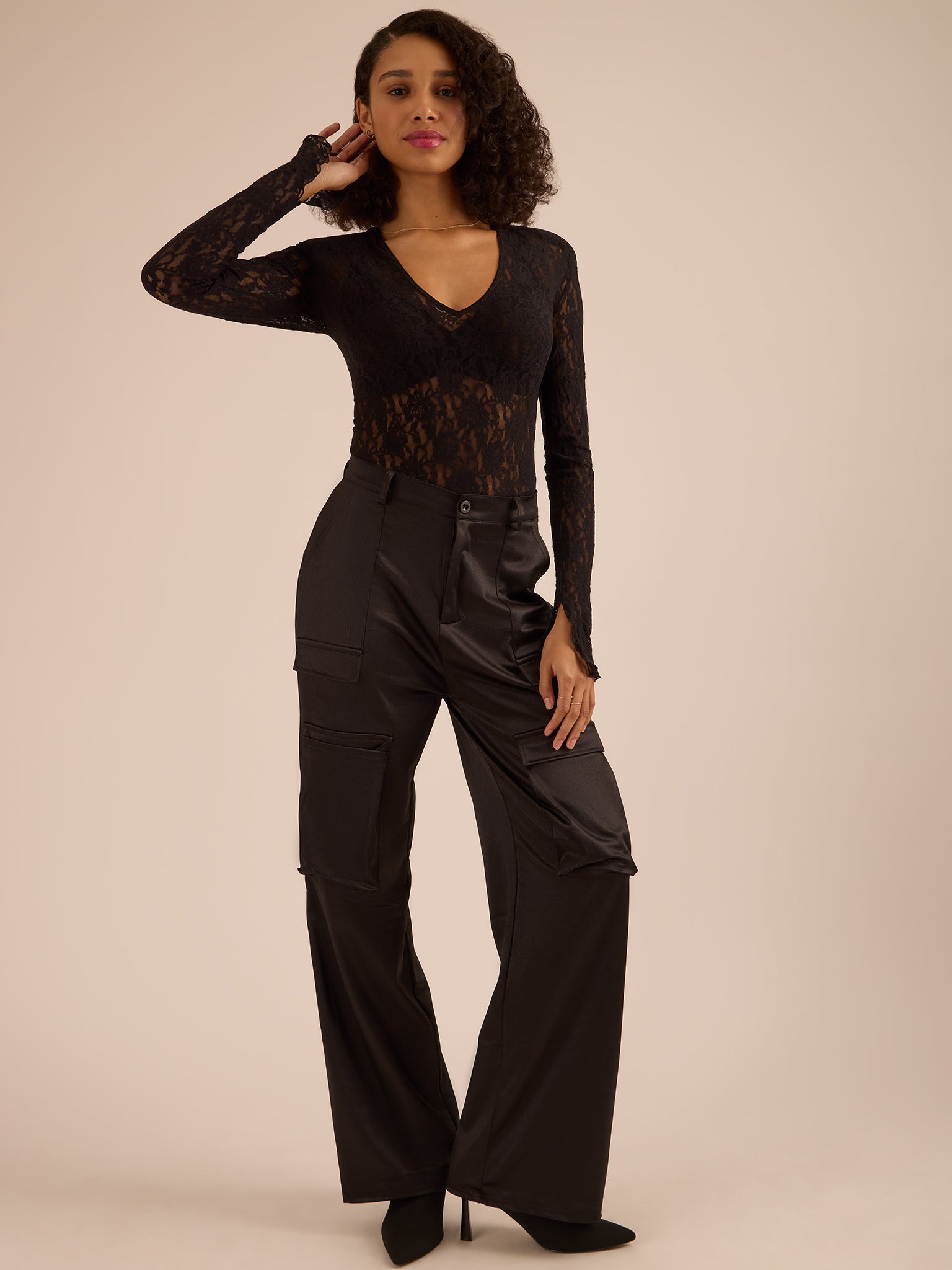 Woman wearing a black lace top and black pants against a beige background