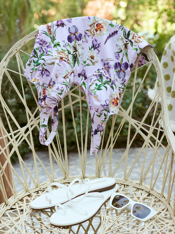Floral-patterned baby romper on a wicker chair with white sandals and sunglasses.