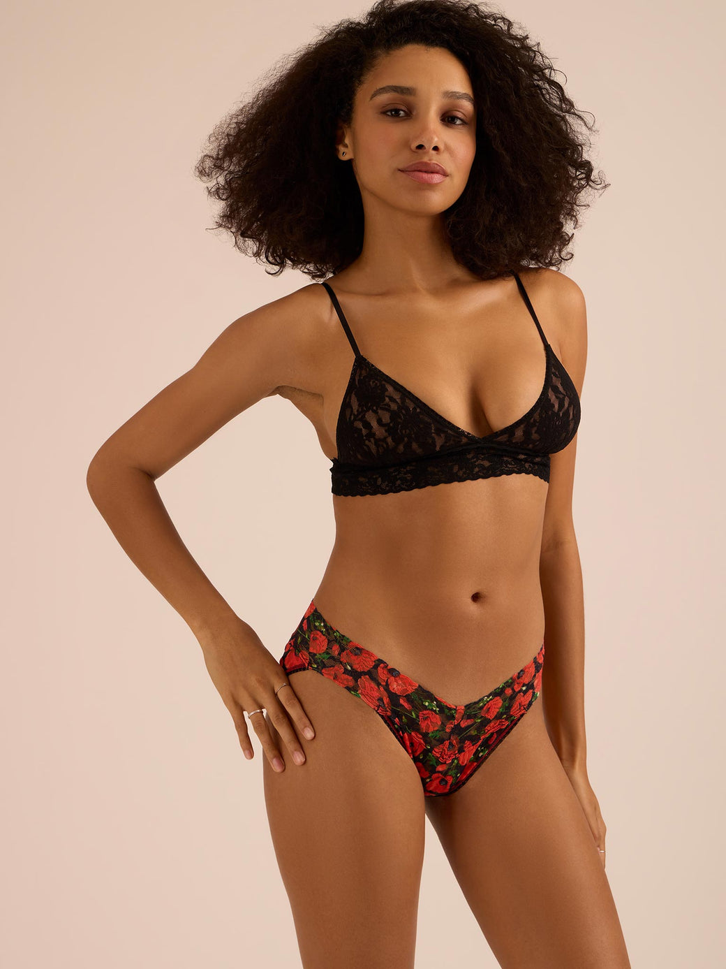 Woman wearing a black lace bra and red floral v-kini bottom on a beige background