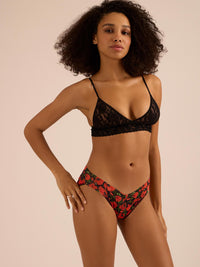 Woman wearing a black lace bra and red floral v-kini bottom on a beige background