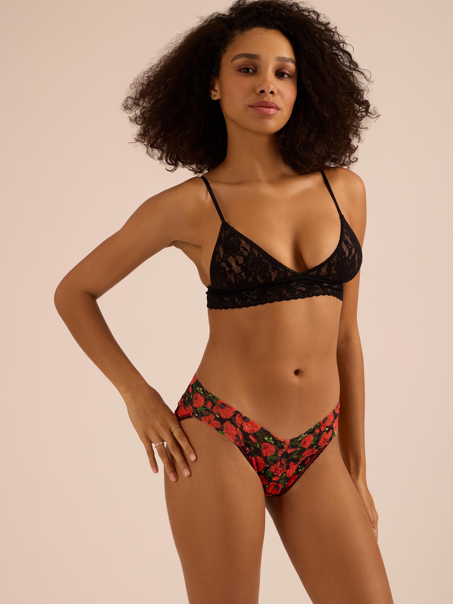 Woman wearing a black lace bra and red floral v-kini bottom on a beige background