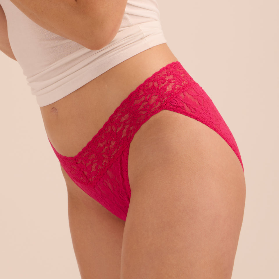 A close-up side view of a person wearing bright magenta lace underwear and a white cropped t-shirt.