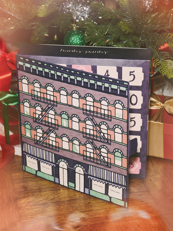 Advent calendar with colorful building design in front of a Christmas tree and presents.