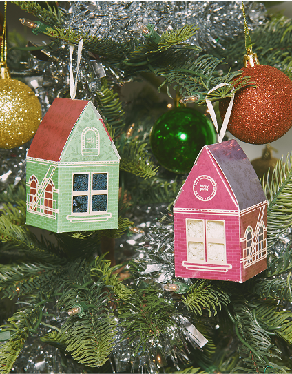 Two house-shaped Christmas ornaments on a tree with other decorations.