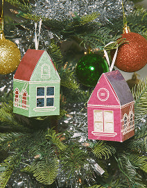 Two small house-shaped Christmas ornaments on a tree with green and red decorations.