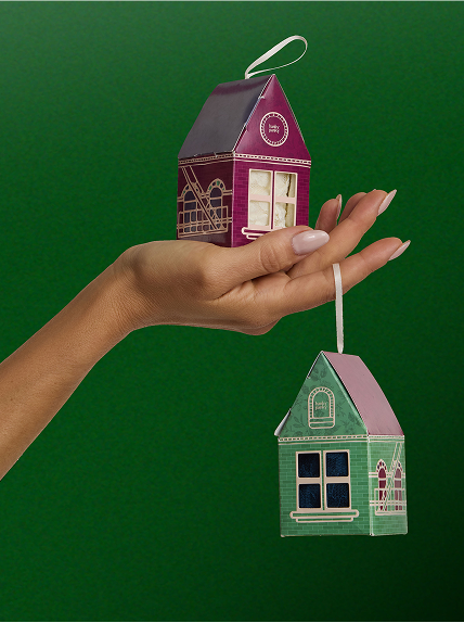 Hand holding a small house-shaped ornament against a green background