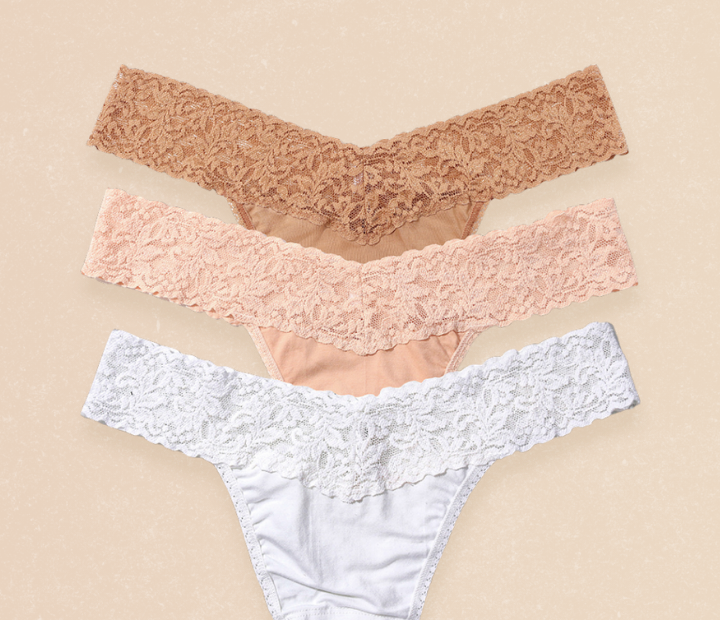 Three pairs of lace underwear in brown, pink, and white on a beige background.